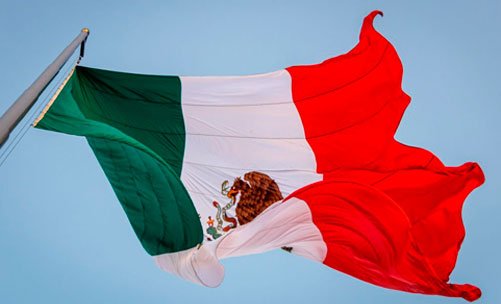 Lábaro patrio ondeando en lo alto bajo el sol en el día de la bandera de México.