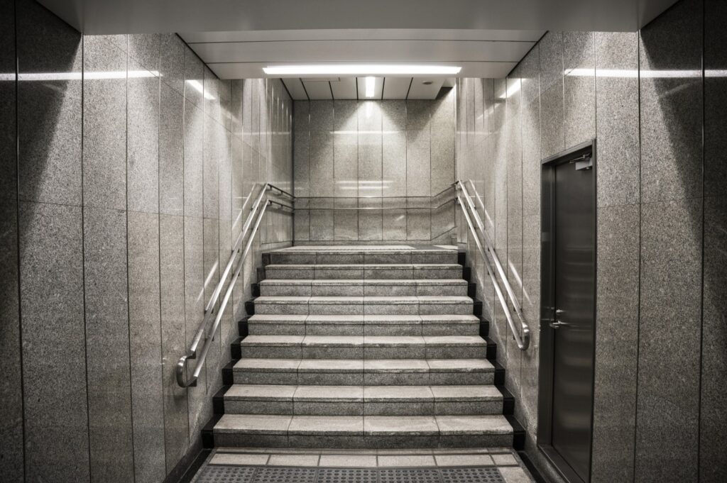 Escalera de concreto con acabados en mármol gris y barandales metálicos en el segundo piso de un edificio de departamentos