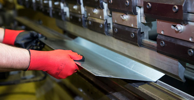 Manos de trabajador con guantes plegando una lámina en una máquina industrial